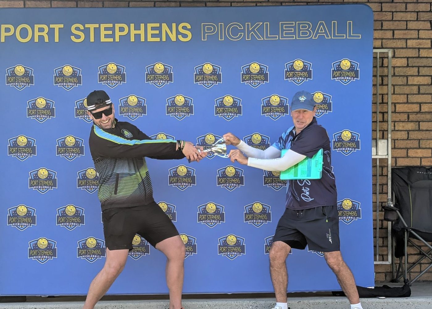 The two club presidents playfully pulling the trophy in opposite directions